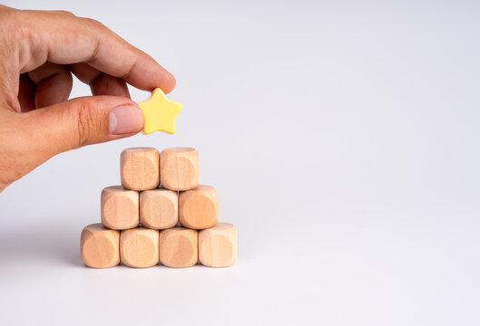 Hand placing yellow star on top of stacked wooden blocks on white background. Achievement, excellence, recognition, business success, employee reward, performance improvement, and quality leadership.