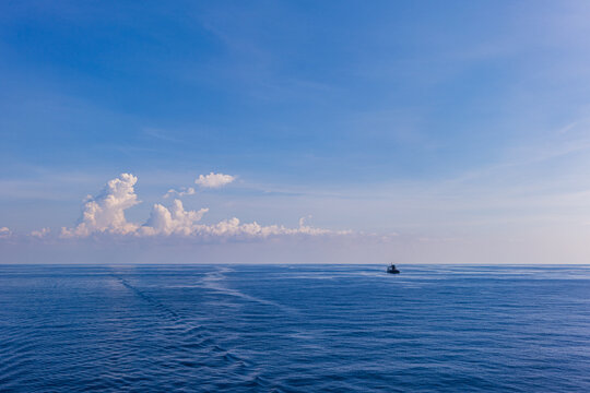 Small vessel crossing calm blue ocean beneath distant clouds