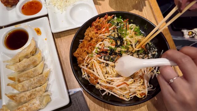 Overhead View of Person Eating Spicy Ramen and Gyoza with Chopsticks