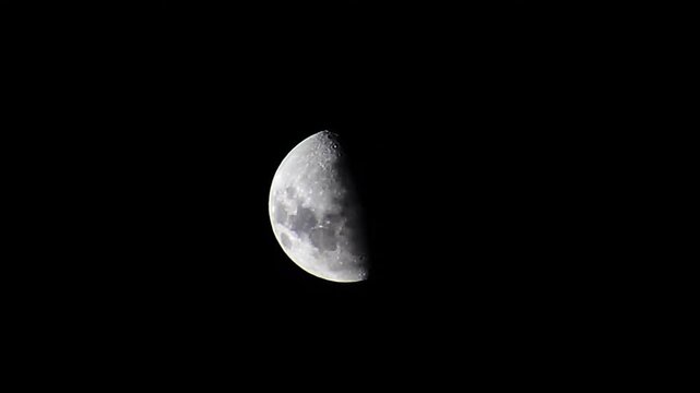 Real first quarter half moon shining bright in the pitch black night sky, detailed lunar surface with craters visible, celestial astronomy telescope shot.