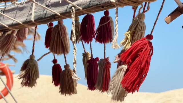 Close Up of Multicolored Decorative Tassels and Rope Knots swaying in the wind on Bedouin Tent Frame with Desert Background