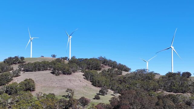 Wind Turbines Spinning on Rural Hillside Under Clear Blue Sky