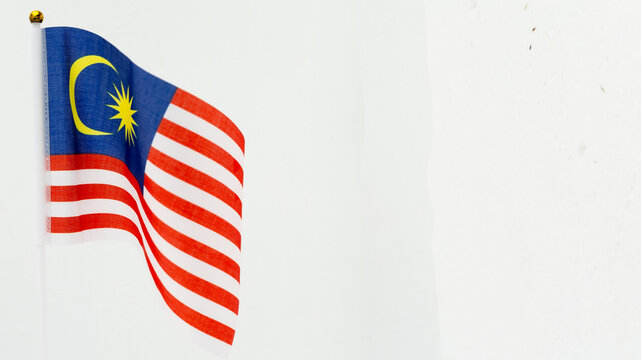 A vibrant Malaysian national flag (Jalur Gemilang) waving gracefully against a clean white wall with ample copy space.