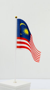 A vibrant Malaysian national flag (Jalur Gemilang) waving gracefully against a clean white wall with ample copy space.