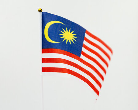A vibrant Malaysian national flag (Jalur Gemilang) waving gracefully against a clean white wall with ample copy space.
