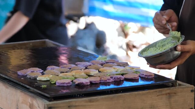 Street vendor pouring and spreading raw coconut batter onto a large heated flat surface to make traditional Thai Khanom Babin pancakes at a market. Thai street food concept