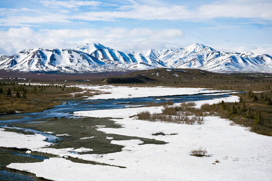 Snowy field with flowing stream and snow covered mountains