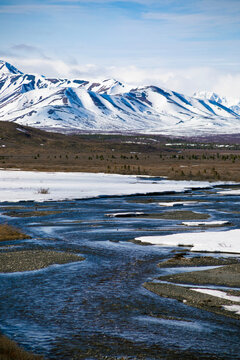 cold, flowing stream in valley with snow covered mountains in the distance