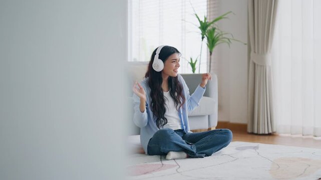 Young asian woman listening to music on couch in living room at home. Happy asia female wearing headset and sitting on the floor