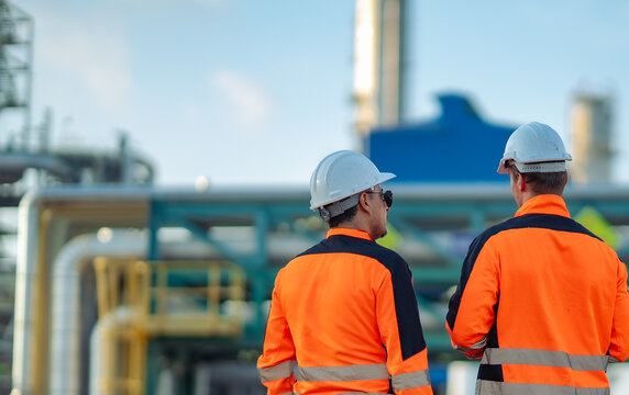 Industrial engineers standing together while reviewing inspection notes on a digital tablet at a refinery. Technical consultation, maintenance planning, engineering teamwork, industrial operations