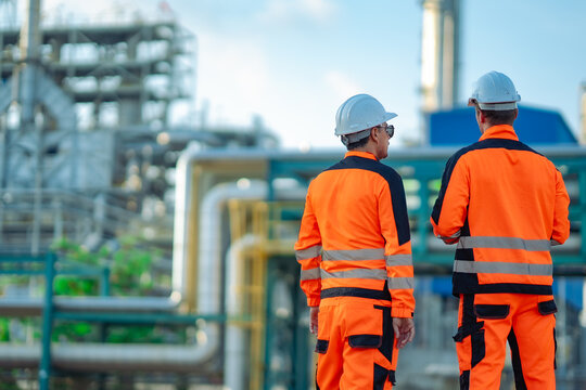 Two industrial engineers pointing toward refinery equipment during a facility inspection. Engineering teamwork, plant assessment, safety compliance, maintenance planning, industrial operations