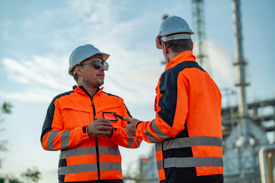 Industrial engineers discussing operational procedures during a refinery inspection. Technical consultation, engineering teamwork, process management, industrial maintenance, energy infrastructure.