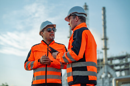 Engineer holding a digital tablet while discussing refinery operations with senior colleague. Industrial planning, engineering consultation, maintenance strategy, production management.