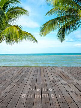 Hello Summer text on wooden deck overlooking tropical beach with palm trees, turquoise sea, and blue sky, perfect for vertical summer background, beach banner, vacation travel and seasonal promotions.