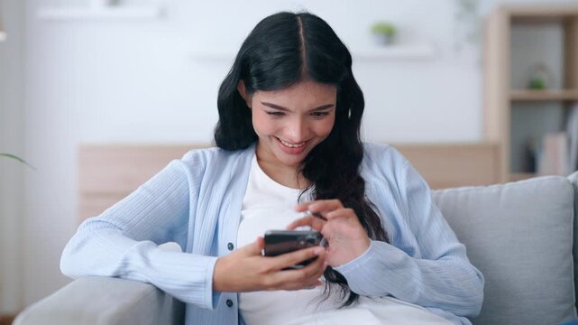Happy young asian woman relax on comfortable couch at home texting messaging on smartphone, smiling girl use cellphone, chatting online message, shopping online from home