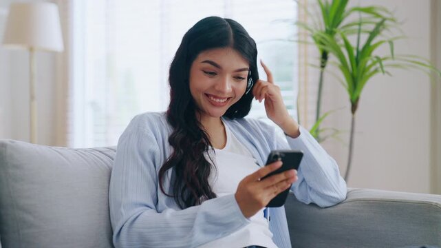 Happy young asian woman relax on comfortable couch at home texting messaging on smartphone, smiling girl use cellphone, chatting online message, shopping online from home