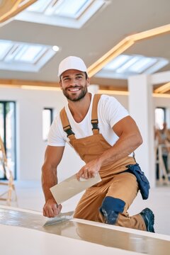 Worker smoothing plaster on wall with trowel in bright modern interior