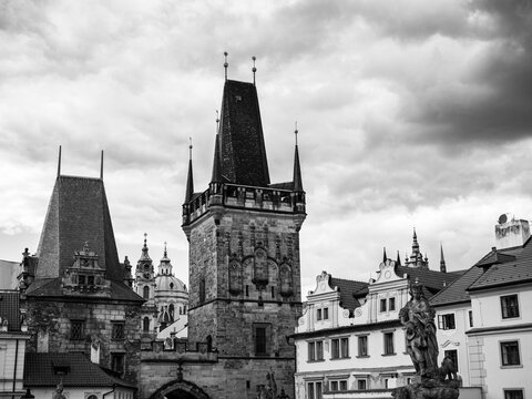 Black and white view of Lesser Town Bridge Tower and Judith Tower near Charles Bridge with St. Nicholas Church and historic buildings in Prague, Czechia.
