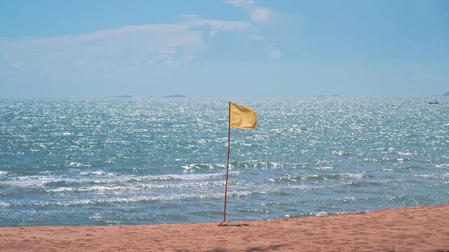 Yellow beach safety flag fluttering on ocean shore under bright blue summer sky.