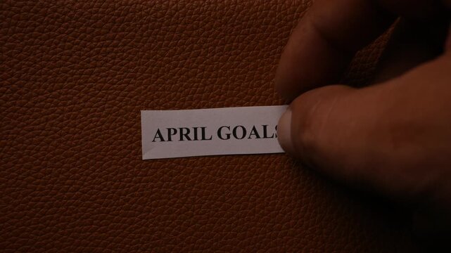 April Goals Text on Tiny Paper Placed on Black Book Background