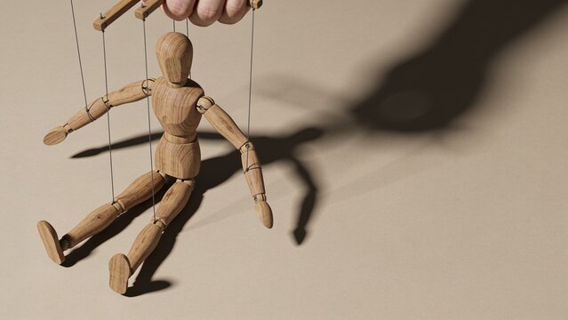 Wooden puppet mannequin controlled by strings casting a dark shadow on a neutral surface.