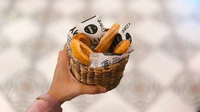 Hand holding a small basket of crispy churros, a traditional fried dough pastry served as a sweet snack.