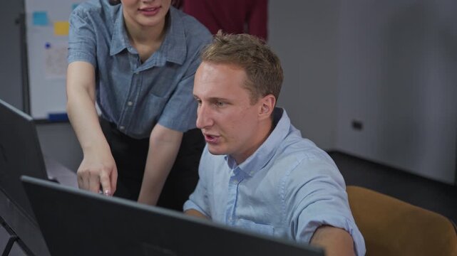 Female developer observes colleague researching AI-assisted solutions on laptop, demonstrating collaborative research methodology and development innovation process.