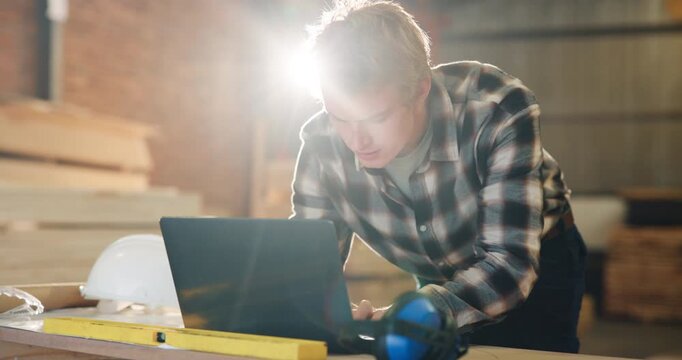 Carpenter, typing and man on laptop in workshop for furniture order, online schedule or email. Carpentry, flare and person on computer for planning, project report or timber inventory for woodworking