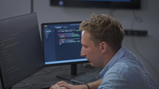 Male developer works with AI-assisted code completion across dual monitors, demonstrating multi-monitor productivity workflow and intelligent development assistance.
