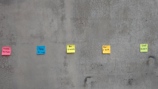 Five Colorful Sticky Notes with Inspirational Messages Stuck on Concrete Wall