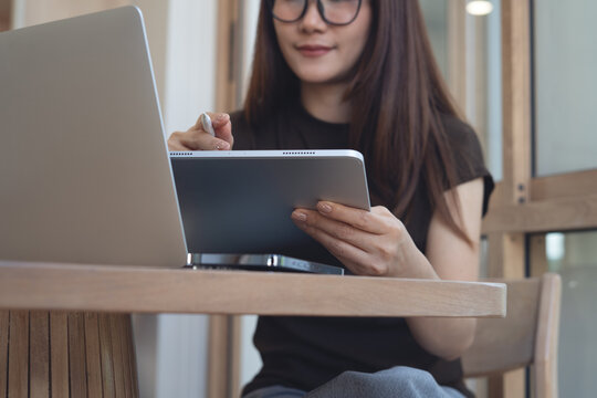 Young asian woman, freelancer using digital tablet while working on laptop computer, surfing the internet at home office. 