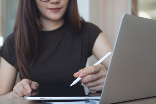 Close up, asian business woman using stylus pen and digital tablet while working on laptop at cafe. Graphic designer, freelancer remote working, using touchpad at coffee shop