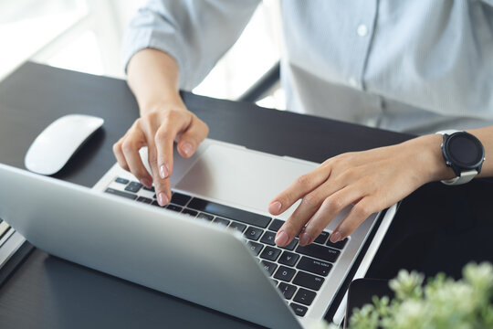 Close up of woman typing on laptop computer with wireless mouse and tablet on desk, working in modern office