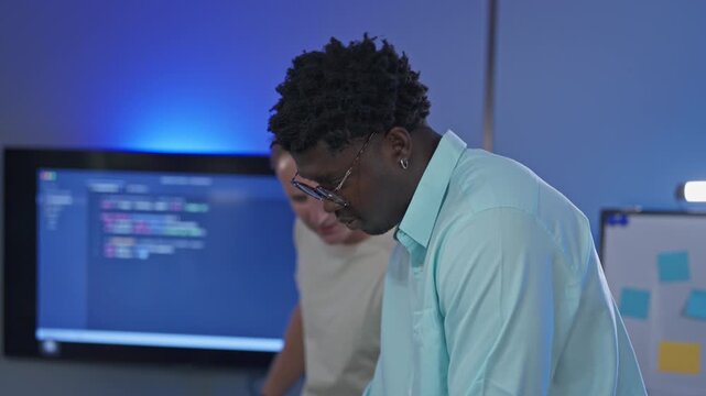African male developer examines code closely for debugging and error investigation, utilizing AI-powered analysis tools for deep problem-solving and code troubleshooting.
