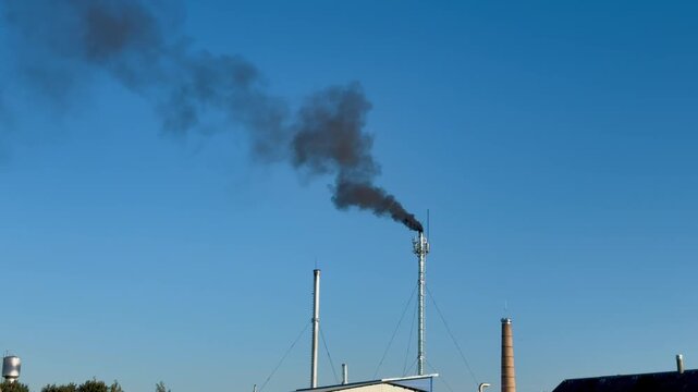 Black smoke spewing from industrial smokestack against clear blue sky