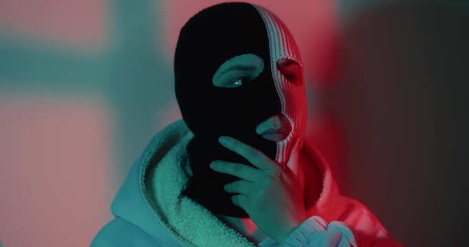 Woman wearing two tone balaclava covering her face. Girl in ski mask posing under red and blue light. Concept of mystery, anonymity and street fashion style.
