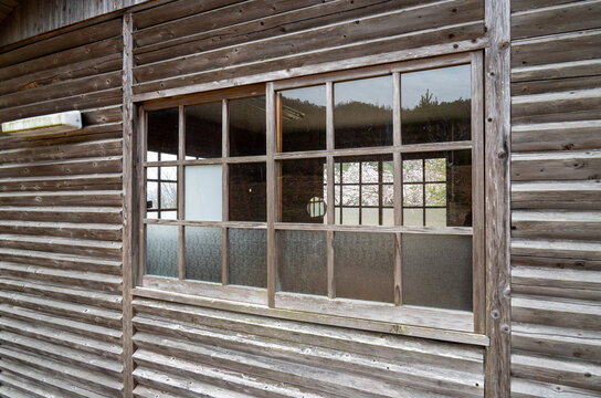Close-up of a rustic wooden building wall with a vintage grid-pane sliding window reflecting spring scenery
