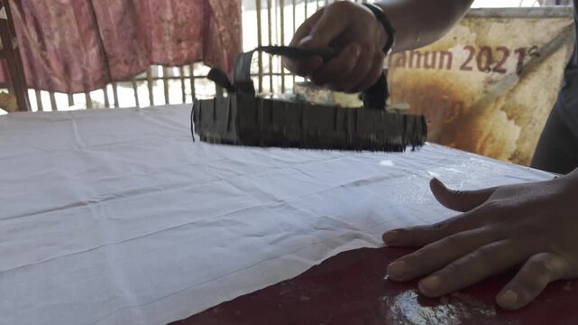 Close Up of Artisan Applying Hot Wax with Copper Batik Stamp on Fabric in Indonesia