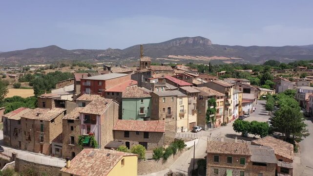 Scenic aerial view of ancient Spanish town of Figuerola dOrcau with tile-roofed houses nestled together on top of hill against mountain range on horizon on sunny summer day, Catalonia