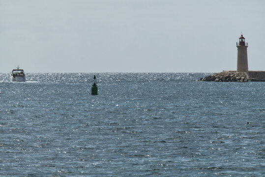 Hafeneinfahrt mit Leuchtturm, Boot und Boje auf dem glitzernden Meer
