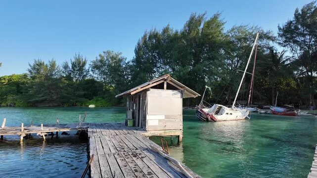 Rustic Wooden Pier and Beach Hut with Sailboat in Crystal Clear Water at Karimunjawa Indonesia
