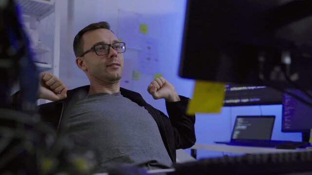 Tired programmer stretching arms at computer desk in office