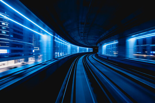 A curved modern subway tunnel with parallel tracks, blue lighting, and a platform, showing a sense of motion and urban transport infrastructure.