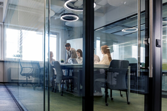 Creative business people, planning and meeting and brainstorming, ideas or strategy at office, view from glass wall.