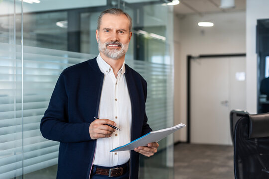 Smiling handsome businessman manager standing in office with documents