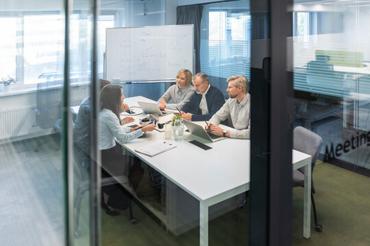 Group of business people standing together and discussing their work and projects, having a team meeting in an office, view from glass wall