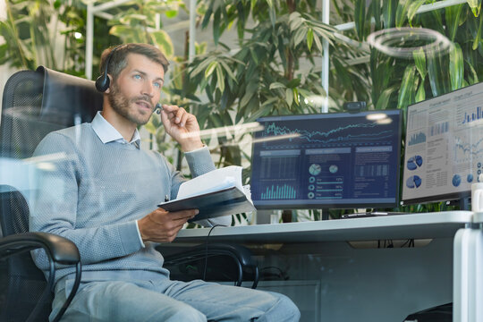 Support service operator talking to customer sitting at desk wearing headset working in modern open space office using PC computer