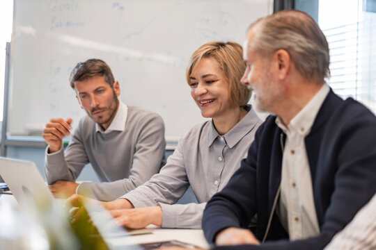 Four business professionals using laptop on desk discussing strategy company