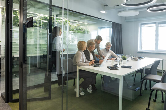 A view through a glass partition shows a modern, busy office interior. Business people are working at desk