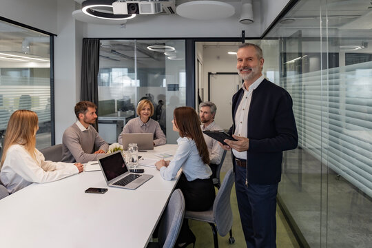 Modern business man in formalwear using digital tablet while standing in the office, colleagues on the background